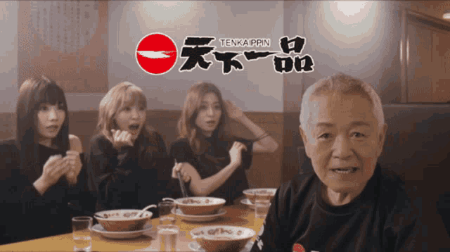 a group of people are sitting at a table with bowls of food in front of a sign that says tenkaippun