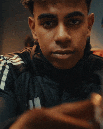 a young man wearing a black adidas jacket looks at the camera