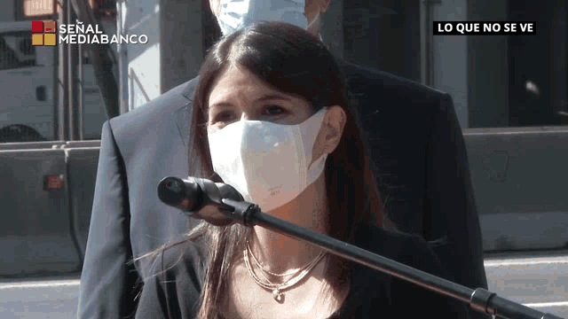 a woman wearing a face mask stands in front of a microphone with the words lo que no se ve on the bottom