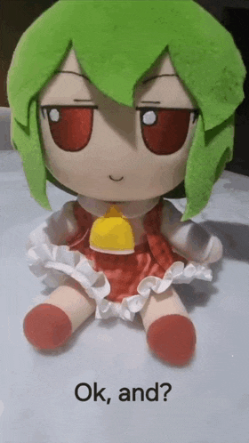 a stuffed doll with green hair and red eyes is sitting on a table with the words `` ok , and ? '' below it .