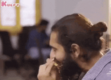 a man with a beard is eating a piece of cake with icing on his face .