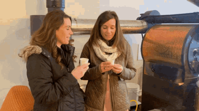 two women standing next to each other holding cups