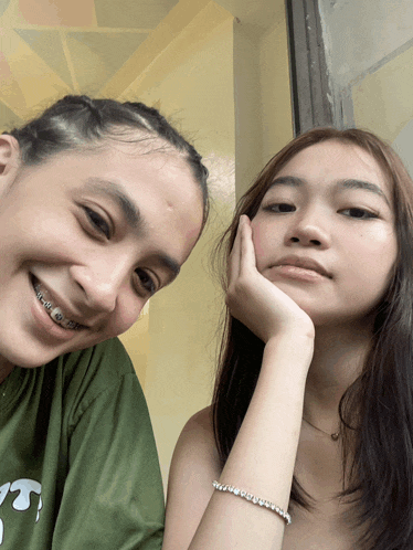 a girl wearing braces smiles next to another girl wearing a bracelet