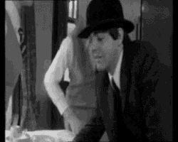a man in a suit and hat is sitting at a table in a restaurant .