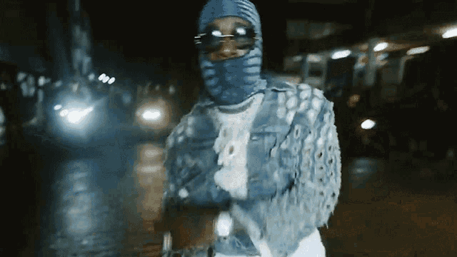 a man wearing a blue ski mask and sunglasses is standing on a street at night .