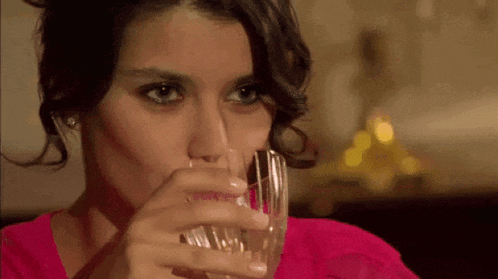 a woman in a pink shirt is drinking from a glass .