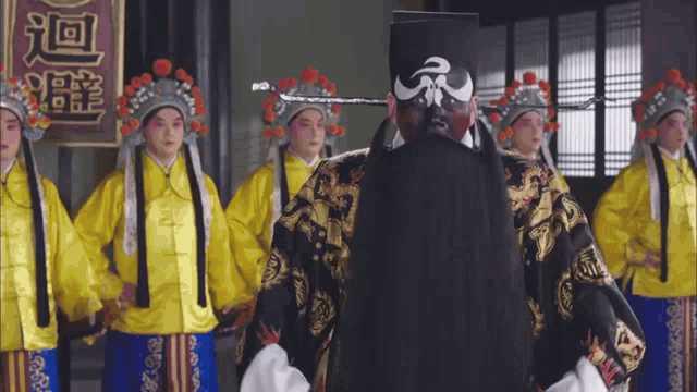 a man in a black hat is standing in front of a group of women in yellow dresses
