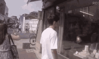 a man in a white shirt is walking down a street next to a store window .