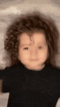 a close up of a baby with curly hair making a funny face .