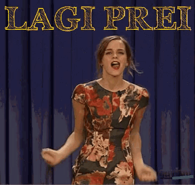 a woman in a floral dress stands in front of a curtain with the words lagi prei written on it