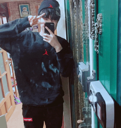 a man taking a picture of himself wearing a supreme sweatshirt and hat