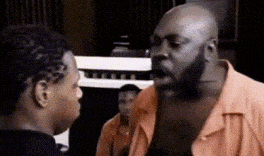 a man and a woman are having a conversation in a room . the man is wearing an orange shirt .