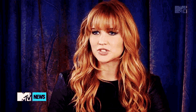 a woman with red hair is sitting in front of a blue curtain with a mtv news logo on it