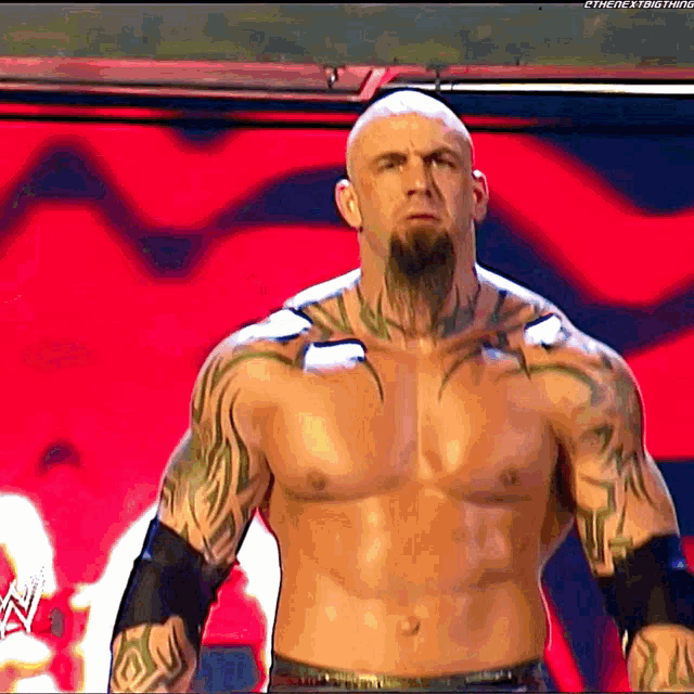 a shirtless wrestler with a beard and tattoos on his chest