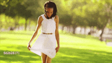 a woman in a white dress is walking in a park with the number 562628171 on the bottom