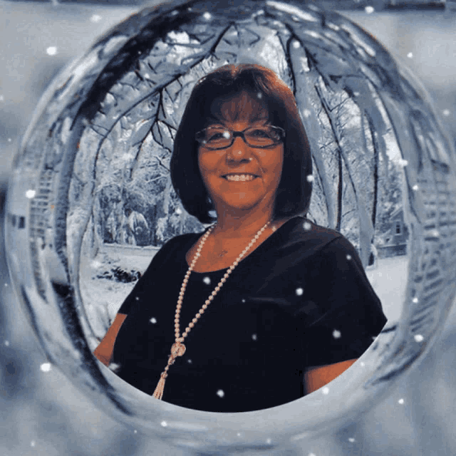a woman wearing glasses and a pearl necklace smiles in a snowy forest