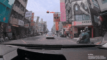 a car driving down a street with a wow tchout logo on the dashboard
