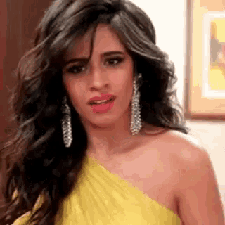 a woman in a yellow dress and silver earrings is making a funny face .