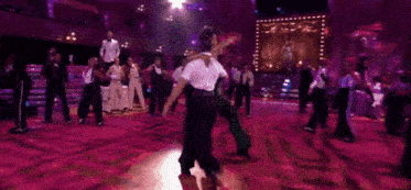 a group of people are dancing on a stage with purple lights behind them