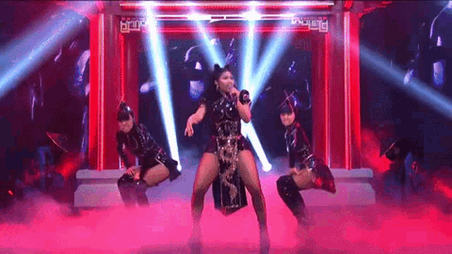 a woman is singing into a microphone on a stage with two dancers