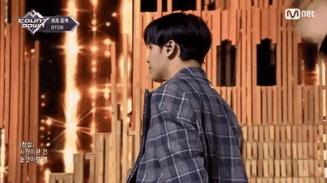 a man in a plaid shirt is standing in front of a wooden wall and a mnet logo .