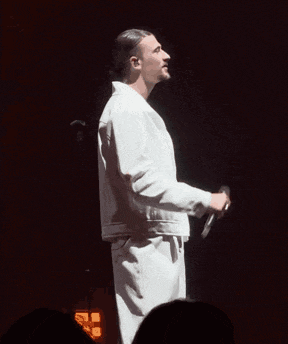 a man in a white jacket is holding a microphone on stage