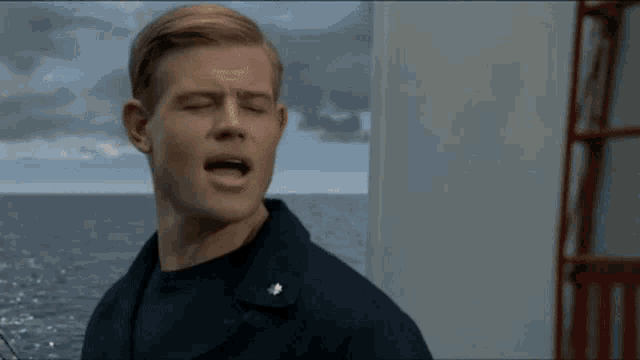 a man in a navy uniform is standing on a boat with his mouth open .