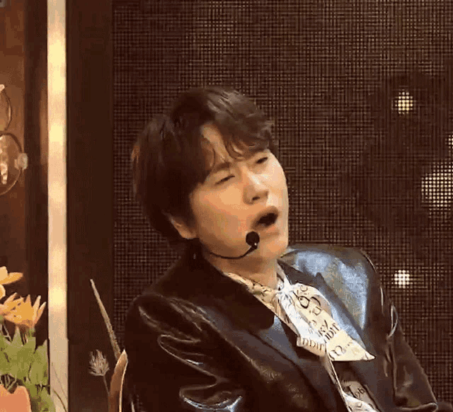 a man wearing a leather jacket and a newspaper shirt is yawning with his mouth open