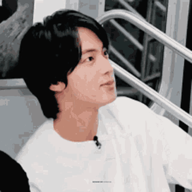 a young man with black hair is wearing a white shirt and sitting on a staircase .