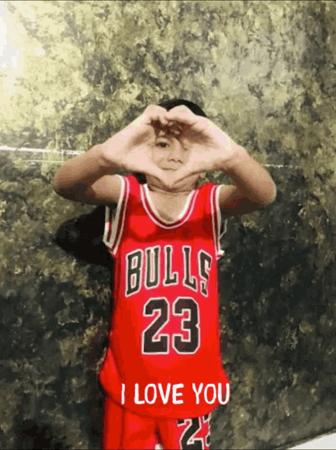 a young boy wearing a bulls 23 jersey makes a heart shape with his hands
