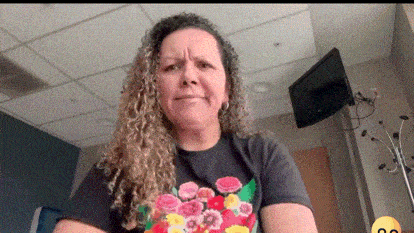 a woman with curly hair is wearing a floral shirt and making a funny face