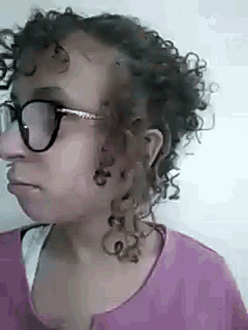 a woman with curly hair wearing glasses and a pink shirt .