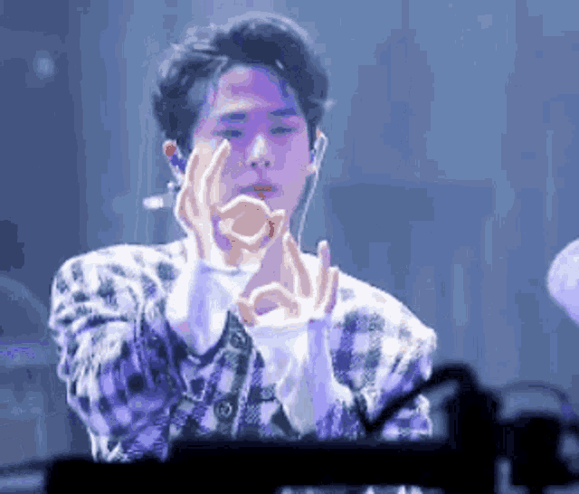 a man in a plaid shirt is making an ok sign with his hands while wearing headphones .