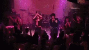 a group of people are standing in front of a stage in a dark room with purple lights .