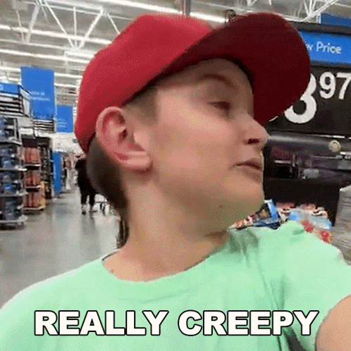 a young boy wearing a red hat and a green shirt is making a really creepy face .