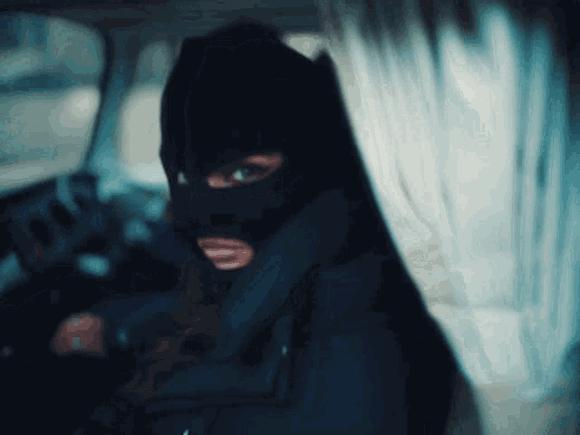 a woman wearing a black ski mask is sitting in a car