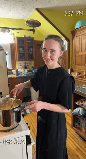 a woman in a black dress is cooking in a kitchen with 6:22 pm on the clock