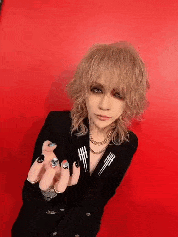 a woman with blonde hair and black nails is wearing a black jacket and necklace .