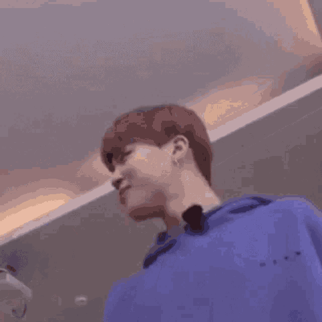 a young man in a blue shirt is standing in a room holding a video game controller .