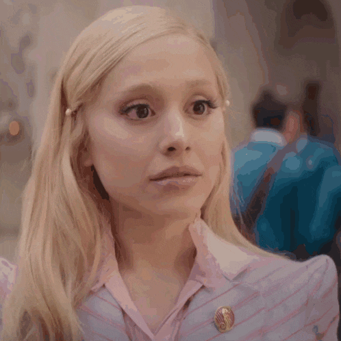 a close up of a woman 's face with blonde hair and a pin on her collar