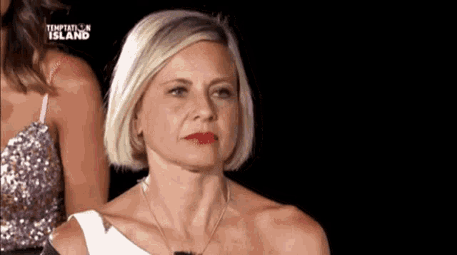 a woman with short blonde hair and red lipstick is standing in front of a woman in a pink dress .