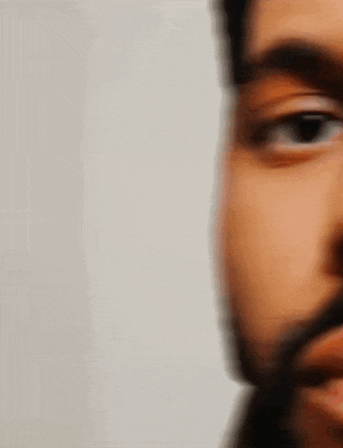 a close up of a man 's face with a beard and black eyes .