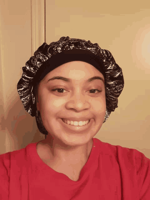 a woman wearing a red shirt and a black and white hat smiles