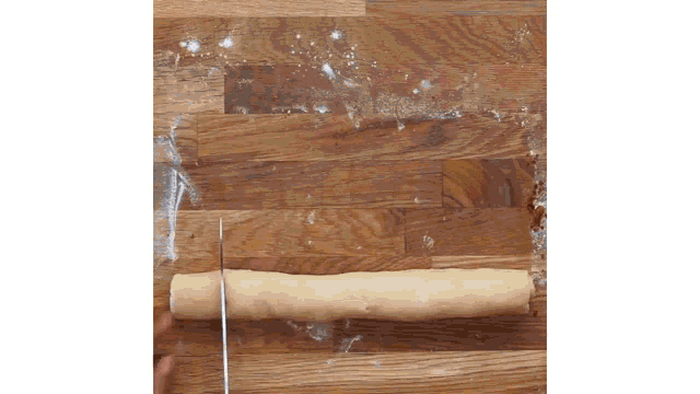 a person is cutting a piece of dough with a knife on a wooden table
