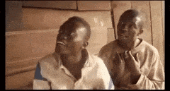 two men are sitting next to each other with their hands on their chests and one of them is smoking a cigarette .