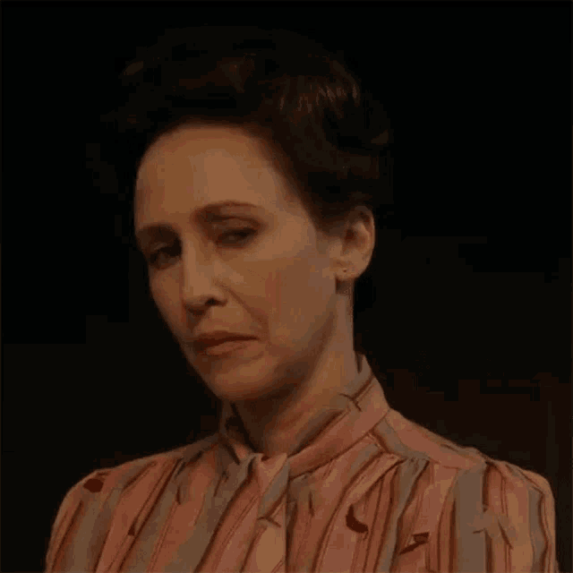 a woman in a pink and gray striped shirt is making a funny face .