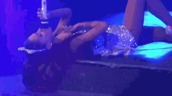 a woman is laying down on a stage holding a microphone
