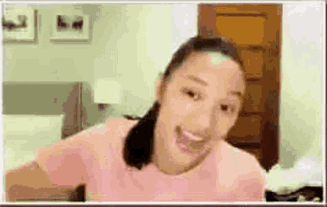 a woman in a pink shirt is making a funny face in a room .