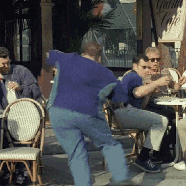 a man in a purple shirt is dancing in front of a sign that says grain cafe