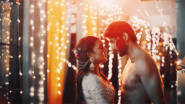 a man and a woman are looking into each other 's eyes in front of christmas lights